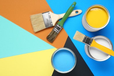 Photo of Cans of colorful paints and brushes on color background, flat lay. Space for text