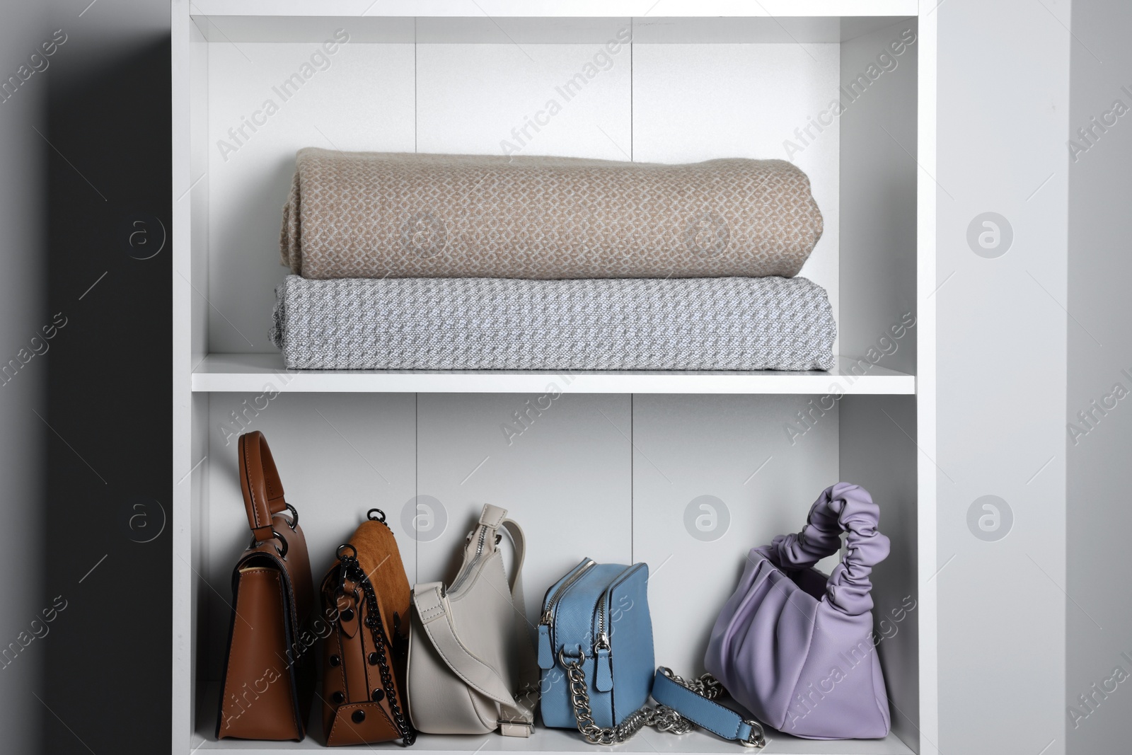 Photo of White shelving unit with rugs and bags in hallway. Interior element