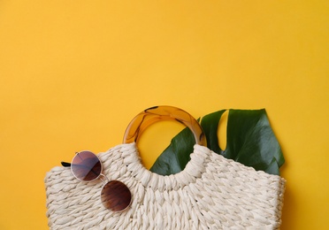Stylish straw bag and sunglasses on yellow background, flat lay with space for text. Summer accessories