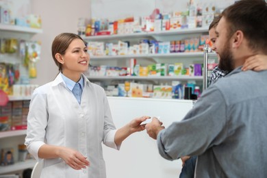 Photo of Professional pharmacist giving pills to customer in modern drugstore