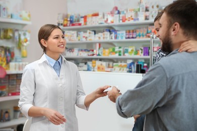 Professional pharmacist giving pills to customer in modern drugstore