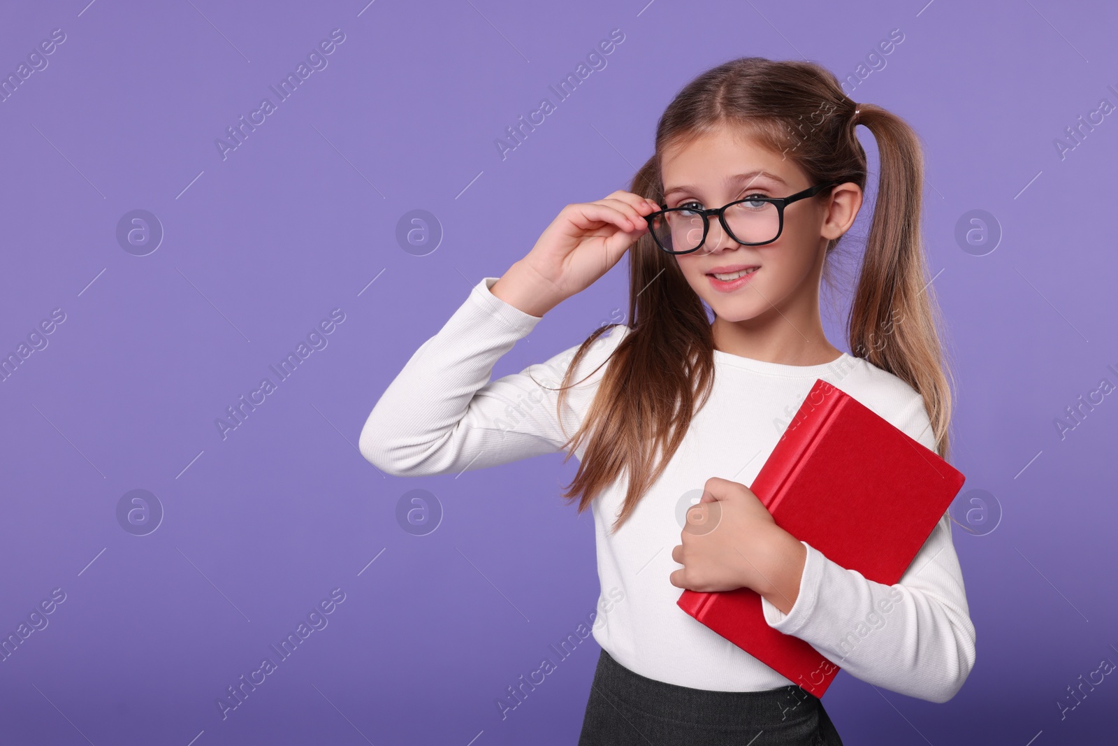Photo of Smiling schoolgirl with book on violet background. Space for text