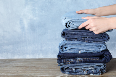 Photo of Woman folding stylish jeans on wooden table, closeup. Space for text