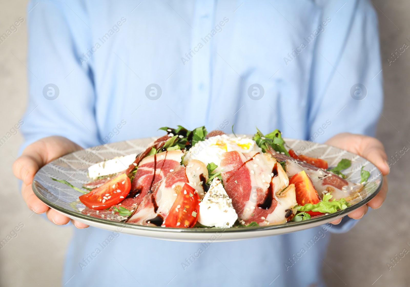 Photo of Woman holding plate with delicious prosciutto salad on grey background, closeup