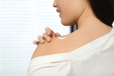 Photo of Young woman applying body cream on shoulder indoors, closeup. Space for text