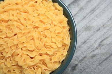 Photo of Raw farfalline pasta in bowl on grey table, top view