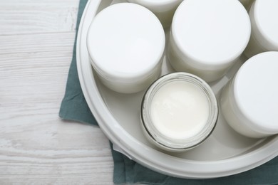 Modern yogurt maker with full jars on white wooden table, top view