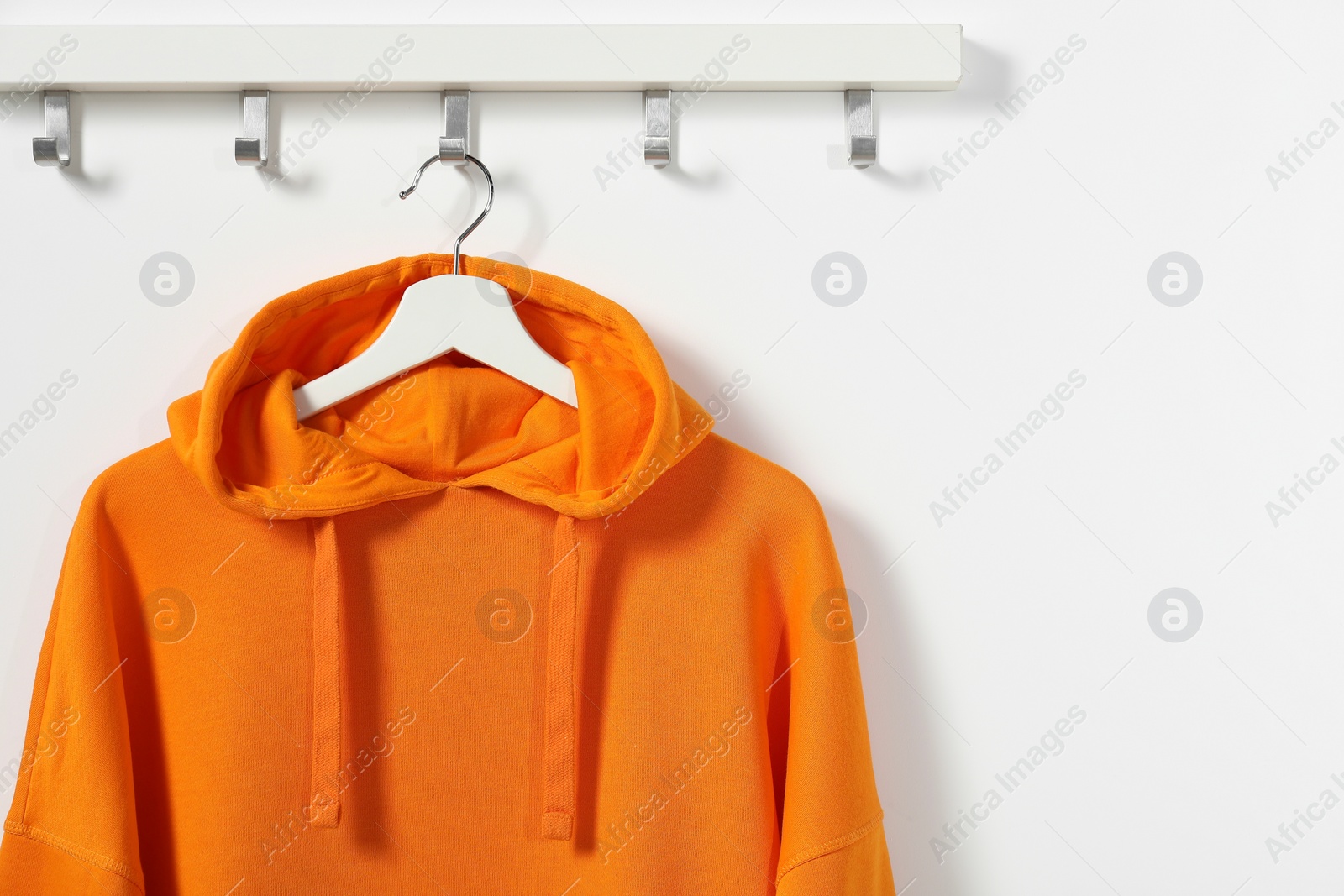 Photo of Hanger with orange hoodie on white wall, space for text