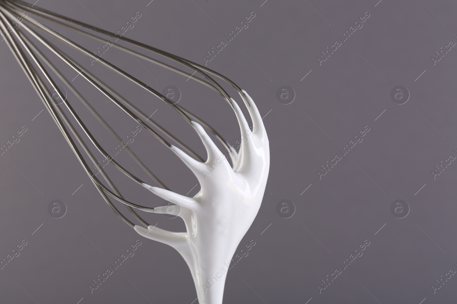 Photo of Whisk with whipped cream on grey background, closeup. Space for text