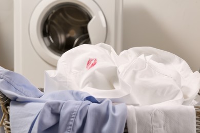 Photo of Men's shirt with lipstick kiss marks among other clothes in laundry basket indoors, closeup