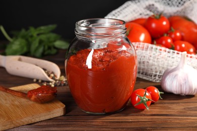 Jar of tasty tomato paste and ingredients on wooden table