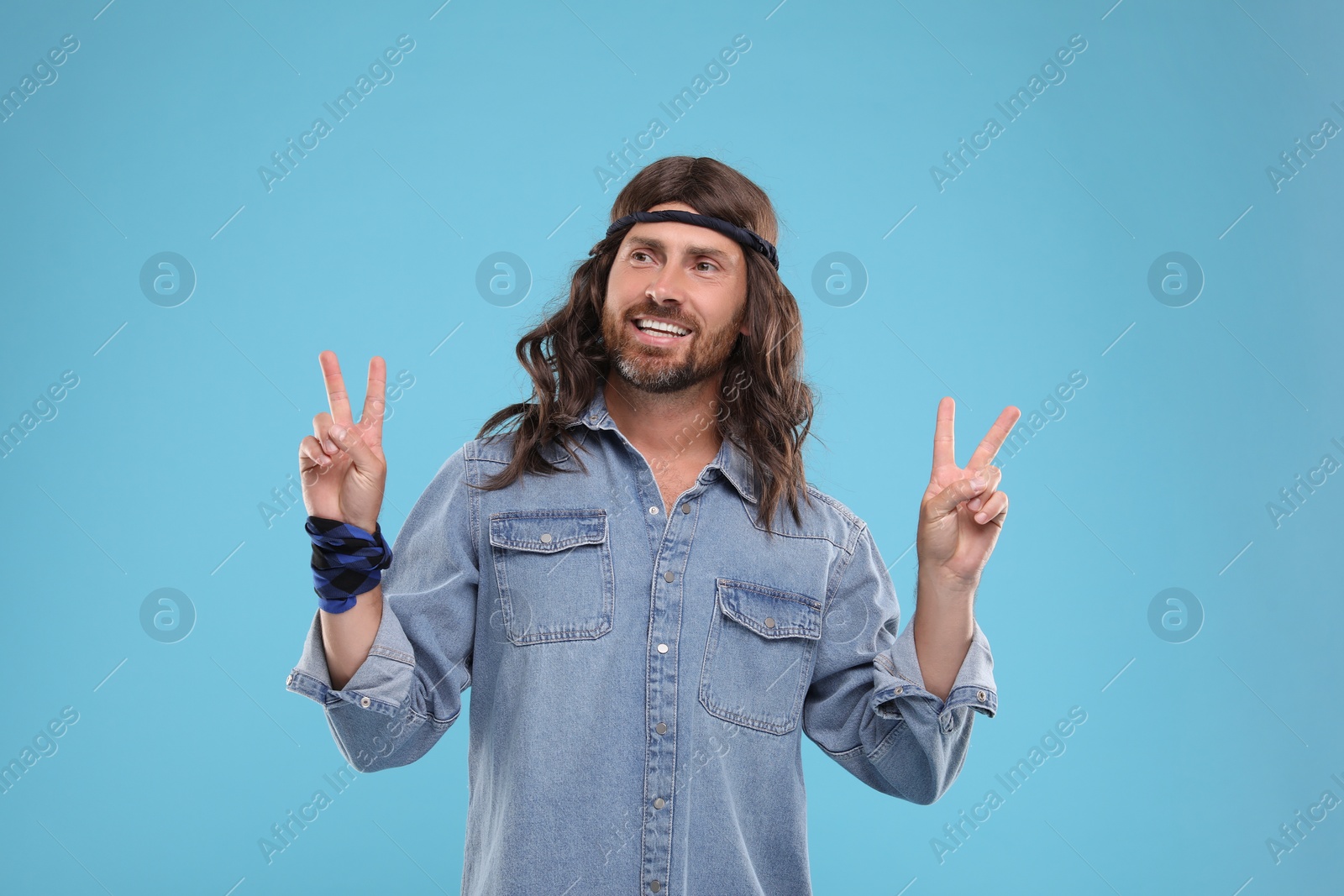 Photo of Stylish hippie man showing V-sign on light blue background