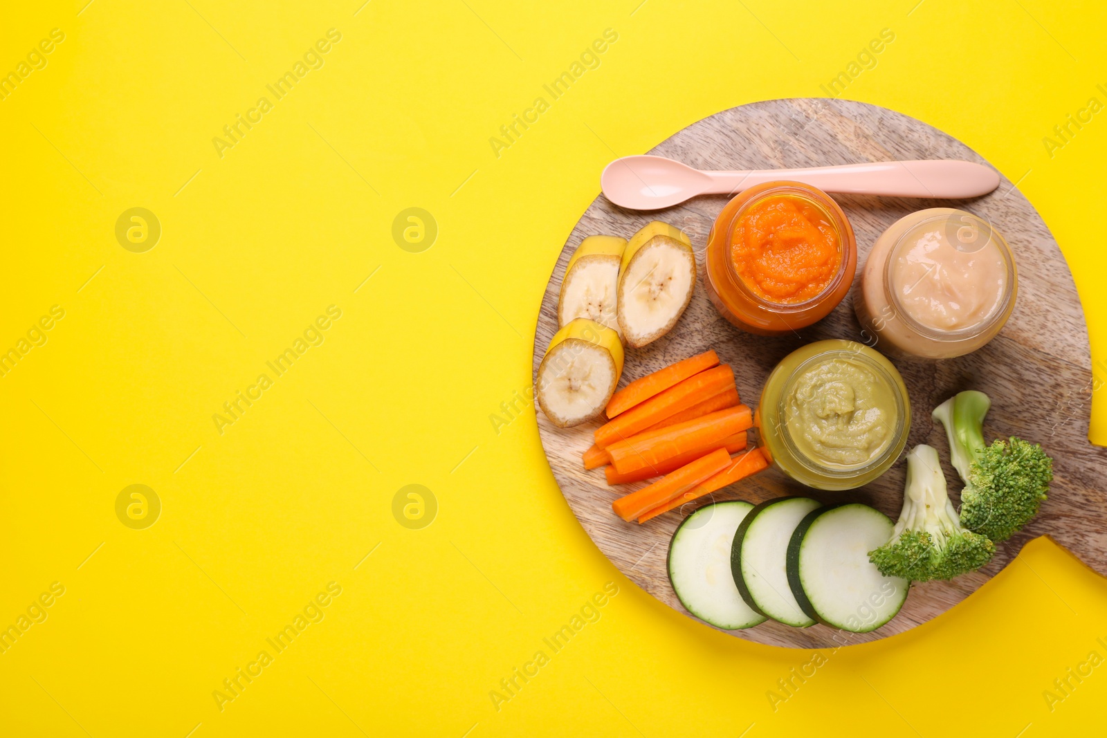 Photo of Glass jars with healthy baby food and ingredients on yellow background, top view. Space for text