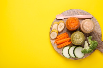 Photo of Glass jars with healthy baby food and ingredients on yellow background, top view. Space for text