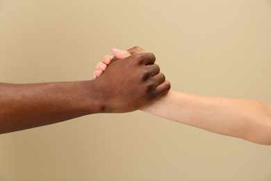 Woman and African American man clasping hands on beige background, closeup