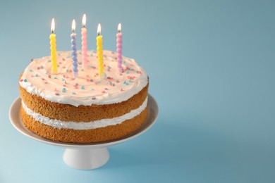 Photo of Tasty cake with colorful candles on light blue background, closeup. Space for text