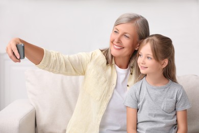 Photo of Happy grandmother taking selfie with her granddaughter at home