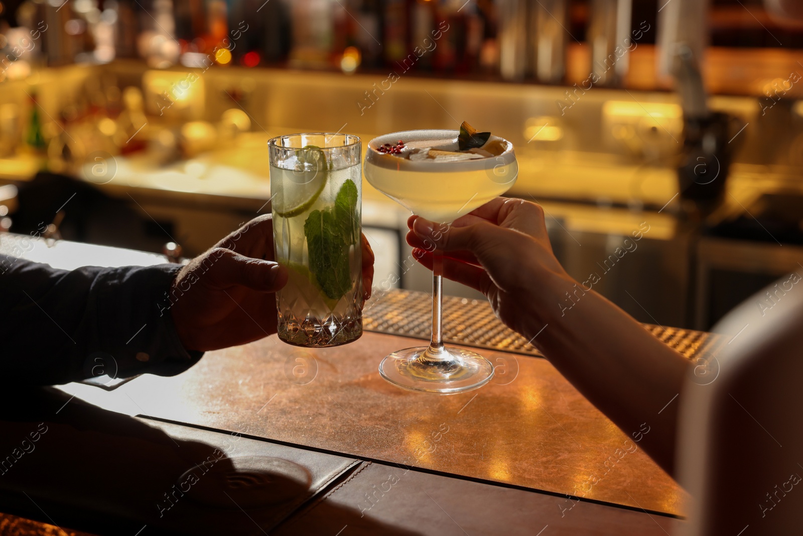 Photo of People clinking glasses with fresh cocktails at bar counter, closeup