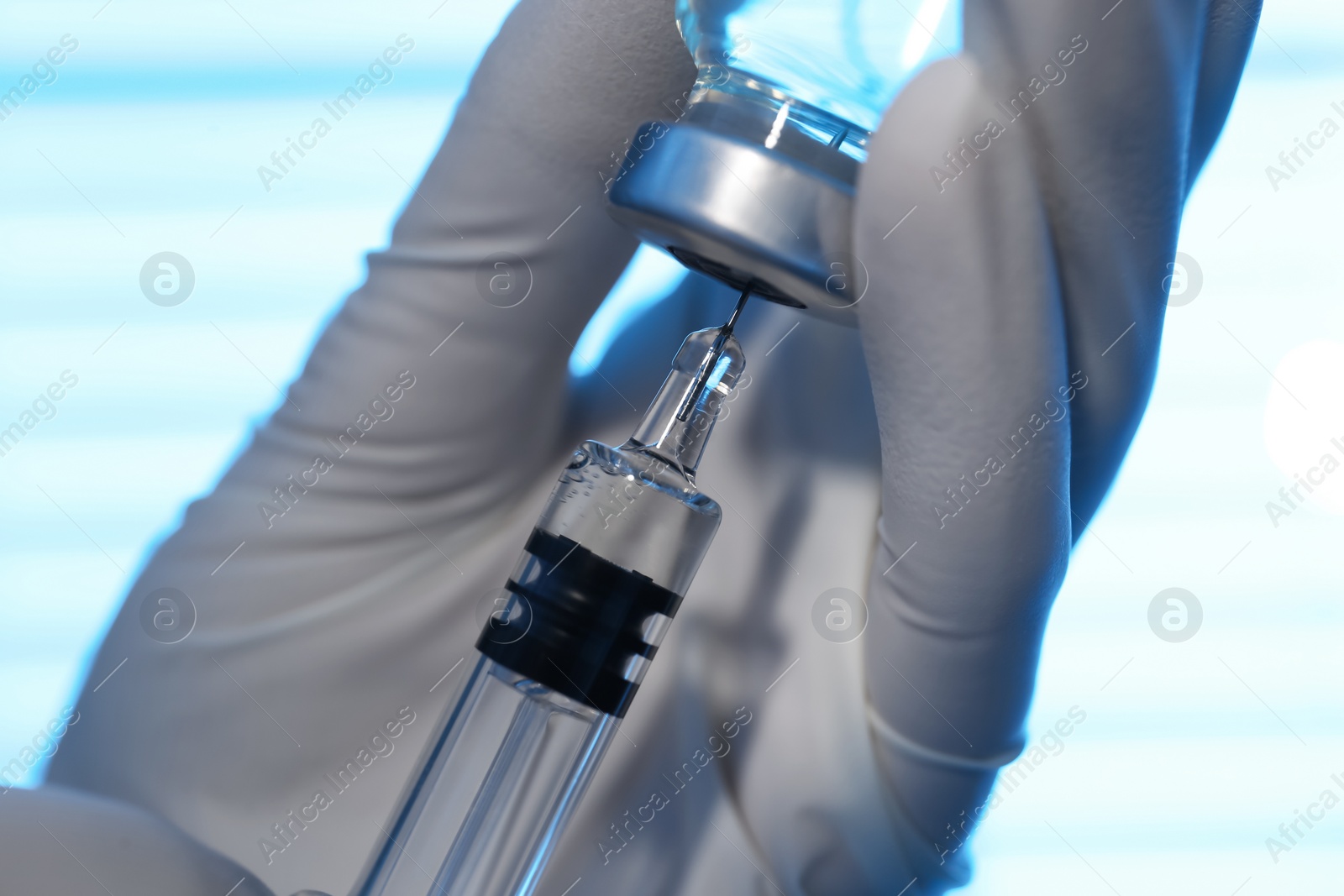 Photo of Woman filling syringe with vaccine from vial on blurred background, closeup