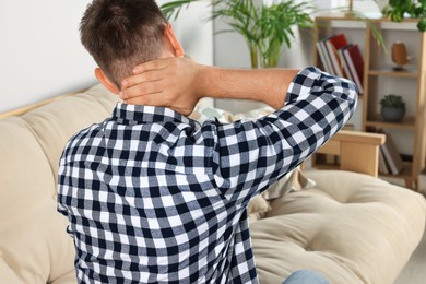 Man suffering from neck pain indoors, back view