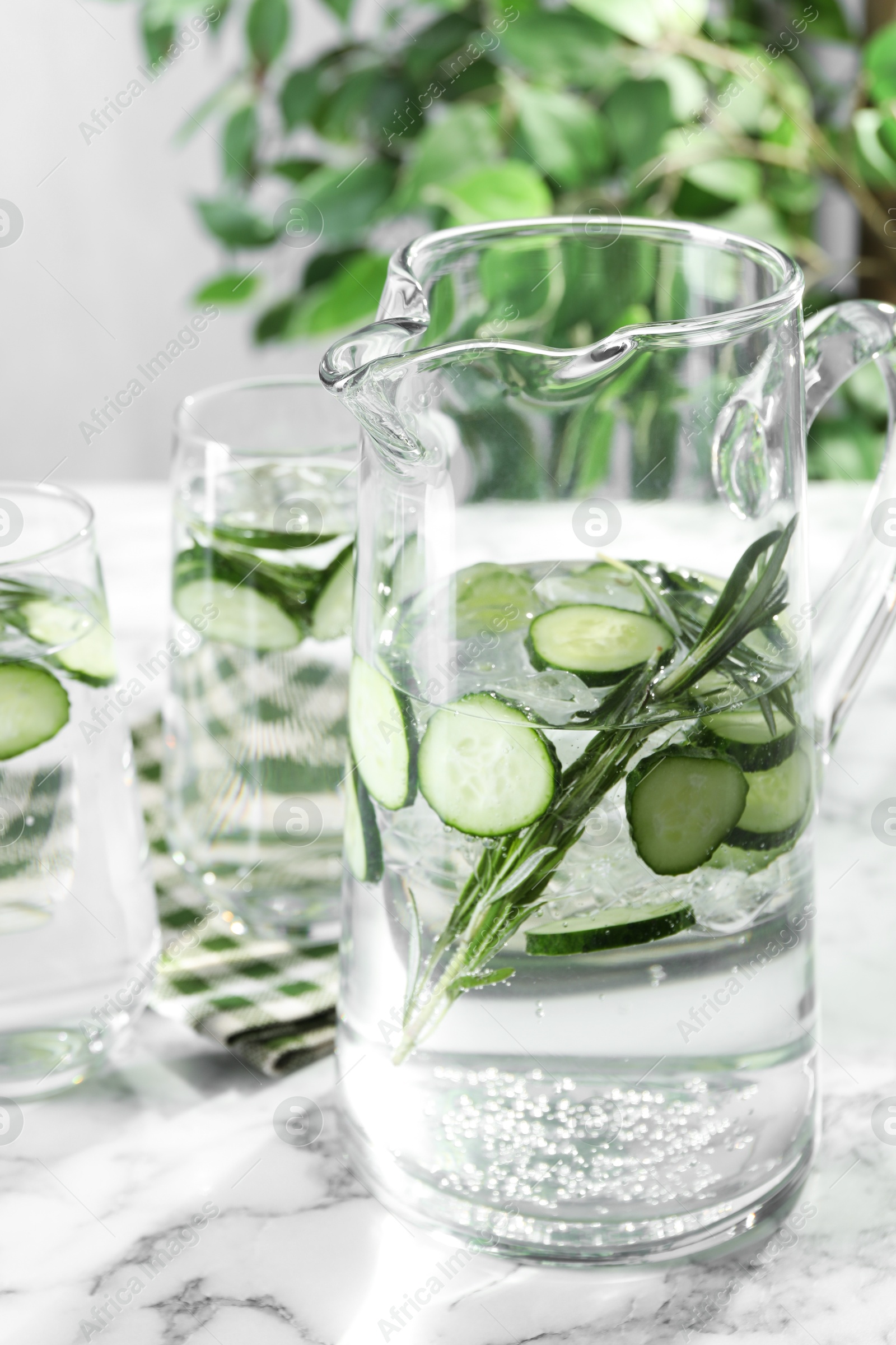 Photo of Refreshing cucumber water with rosemary in jug and glasses on white marble table, closeup