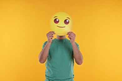 Man covering face with smiling emoticon on yellow background