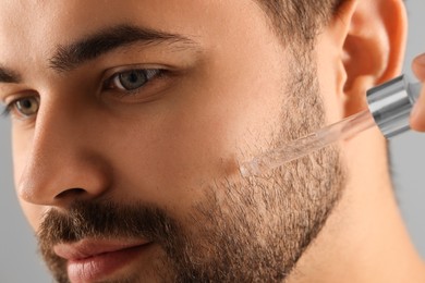 Handsome man applying cosmetic serum onto face, closeup