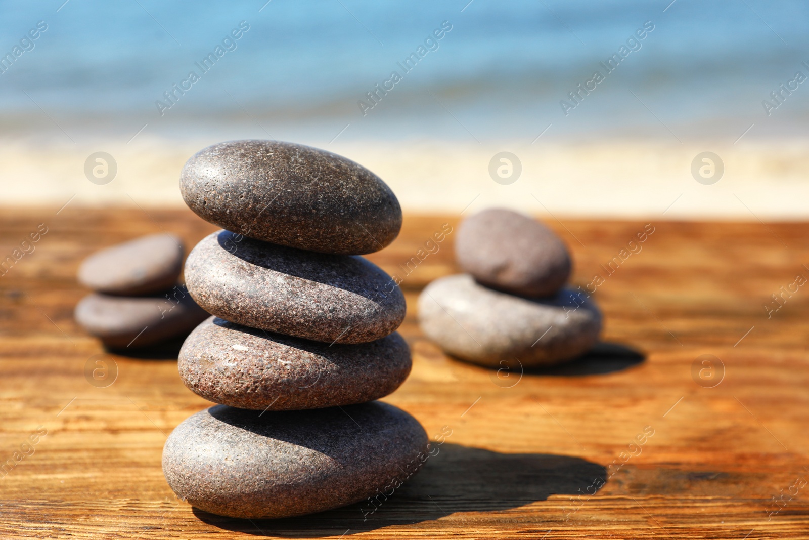 Photo of Stack of stones on wooden table against seascape, space for text. Zen concept