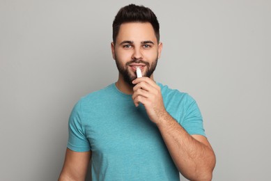 Young man applying lip balm on grey background