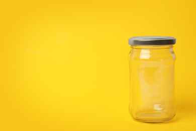 Photo of Closed empty glass jar on yellow background, space for text