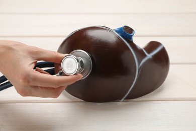 Photo of Doctor with stethoscope examining liver model at white wooden table, closeup