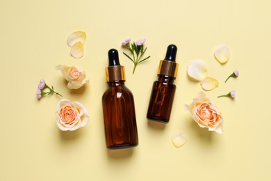 Bottles of cosmetic serum, beautiful flowers and petals on pale yellow background, flat lay