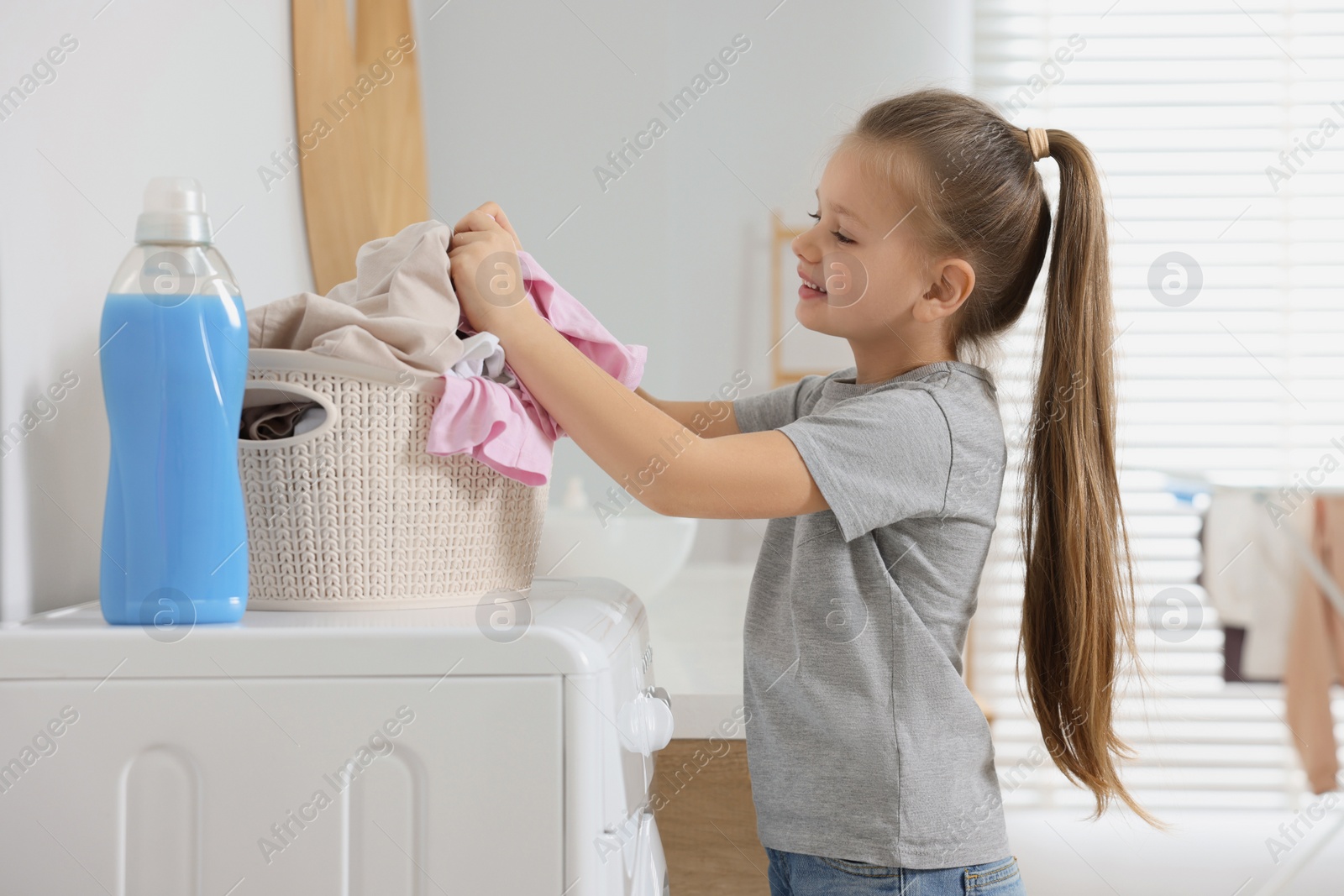 Photo of Little girl taking out dirty clothes from basket in bathroom, space for text