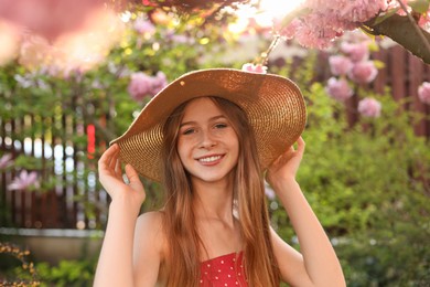 Beautiful teenage girl near blossoming sakura tree in park on sunny day