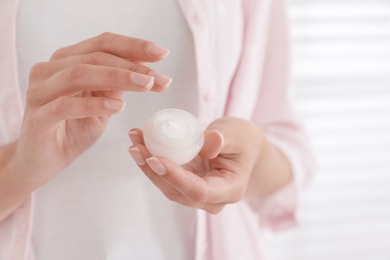 Photo of Woman holding jar with cream near window, closeup