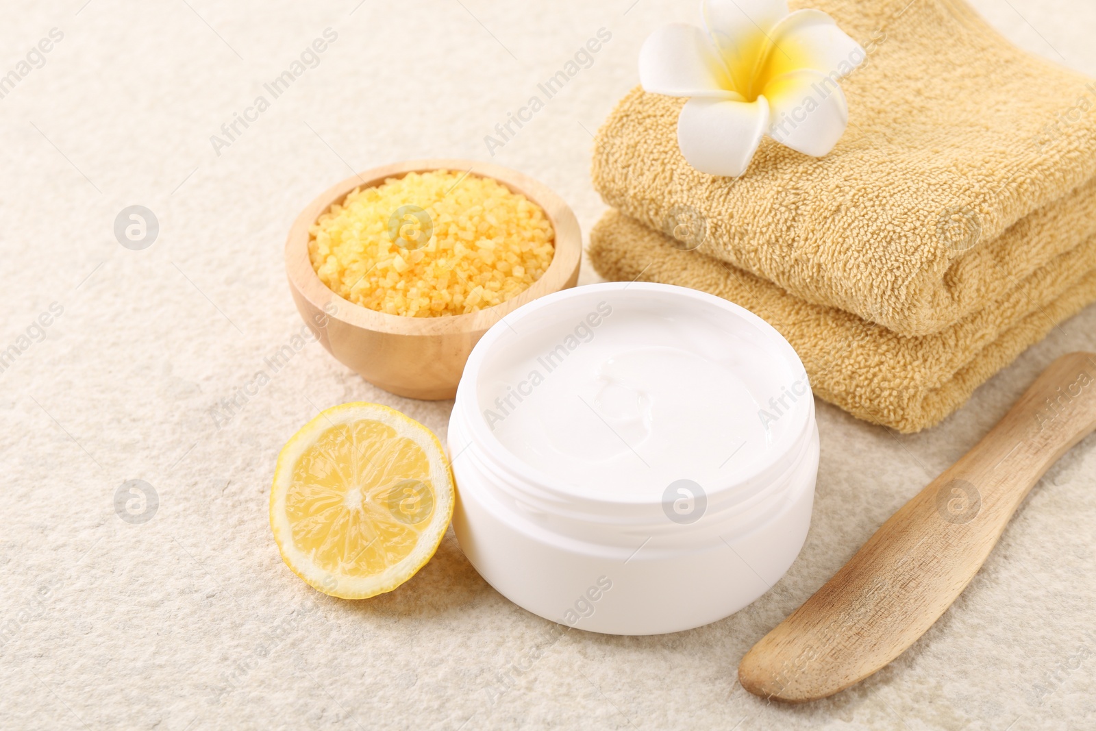 Photo of Body care. Composition with moisturizing cream in open jar and half of lemon on light textured table, closeup