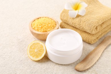 Body care. Composition with moisturizing cream in open jar and half of lemon on light textured table, closeup