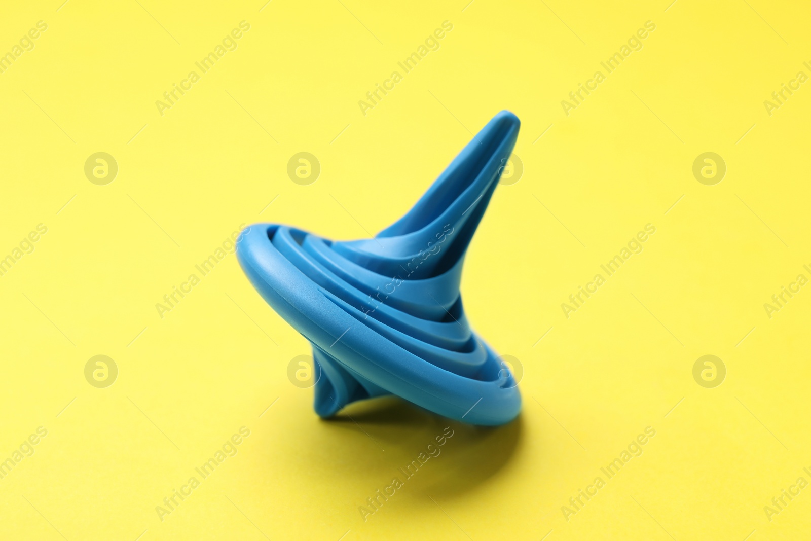 Photo of One blue spinning top on yellow background, closeup