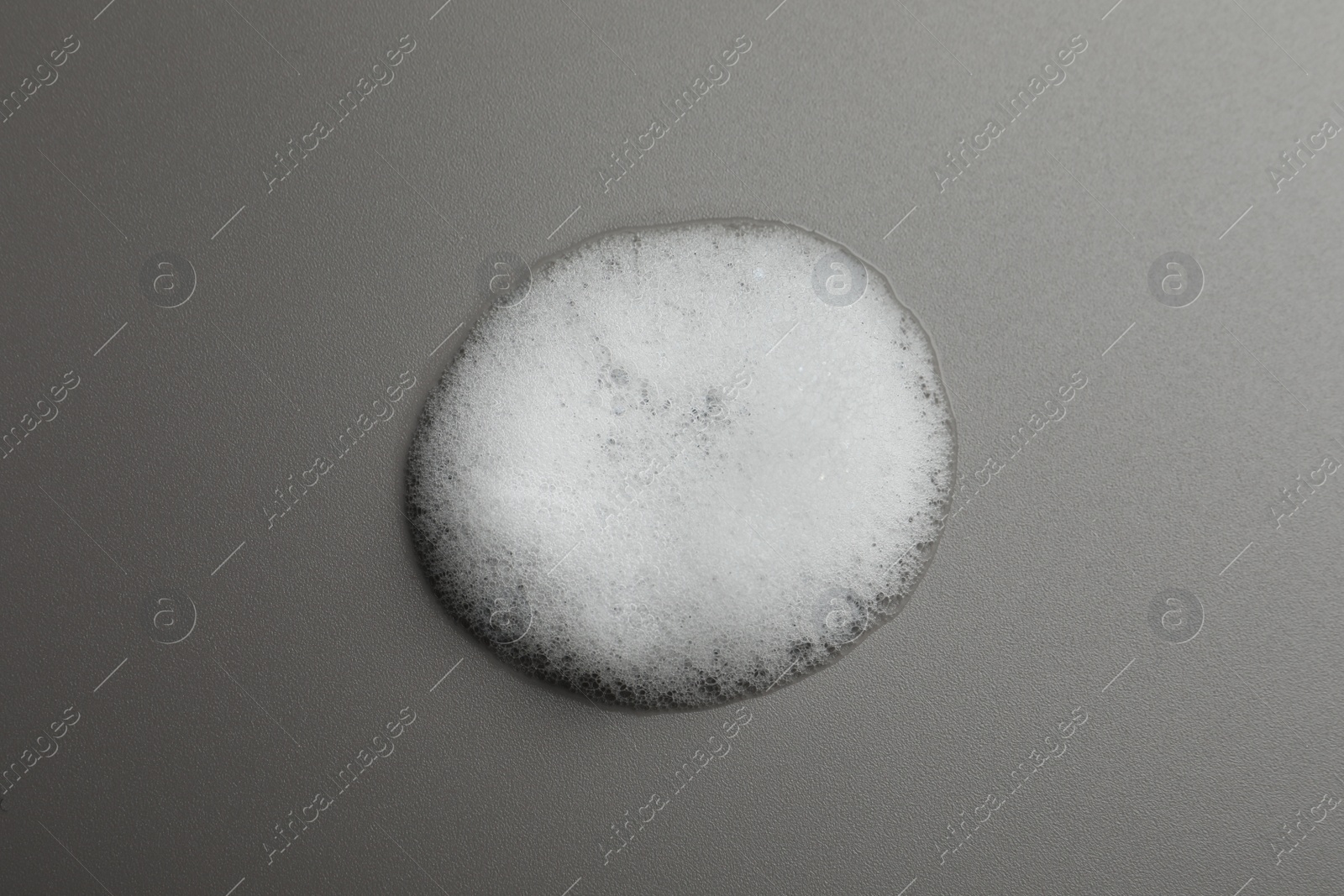 Photo of Drop of fluffy soap foam on grey background, top view