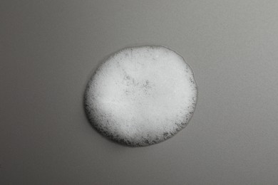 Drop of fluffy soap foam on grey background, top view