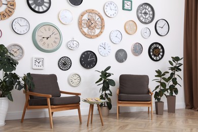 Photo of Comfortable furniture, beautiful houseplants and collection of different clocks on white wall in room