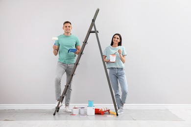 Photo of Young couple with decorator's tools near ladder indoors