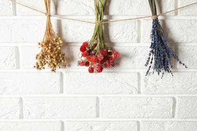 Bunches of beautiful dried flowers hanging on rope near white brick wall. Space for text