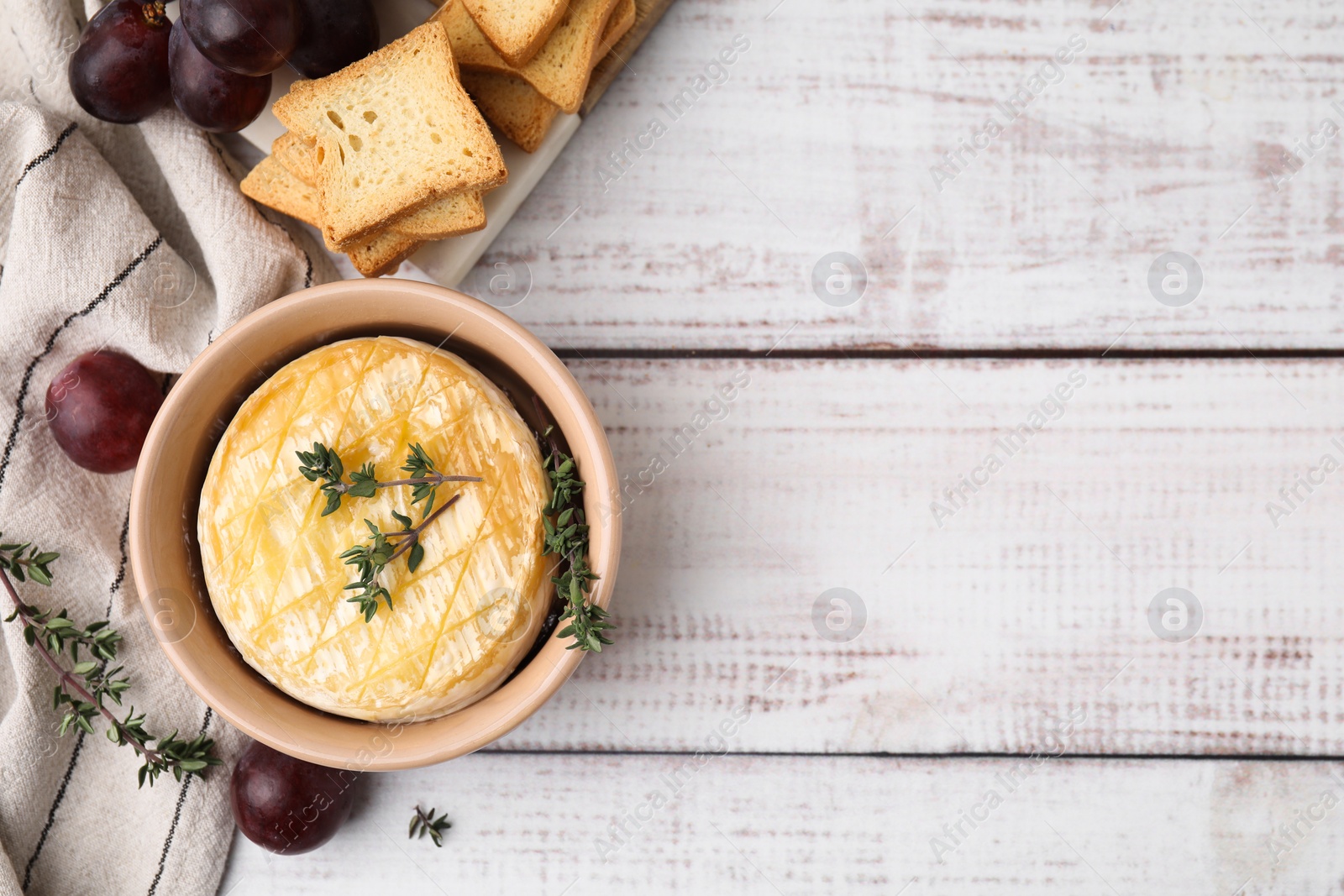 Photo of Tasty baked camembert in bowl, grapes, croutons and thyme on wooden table, flat lay. Space for text