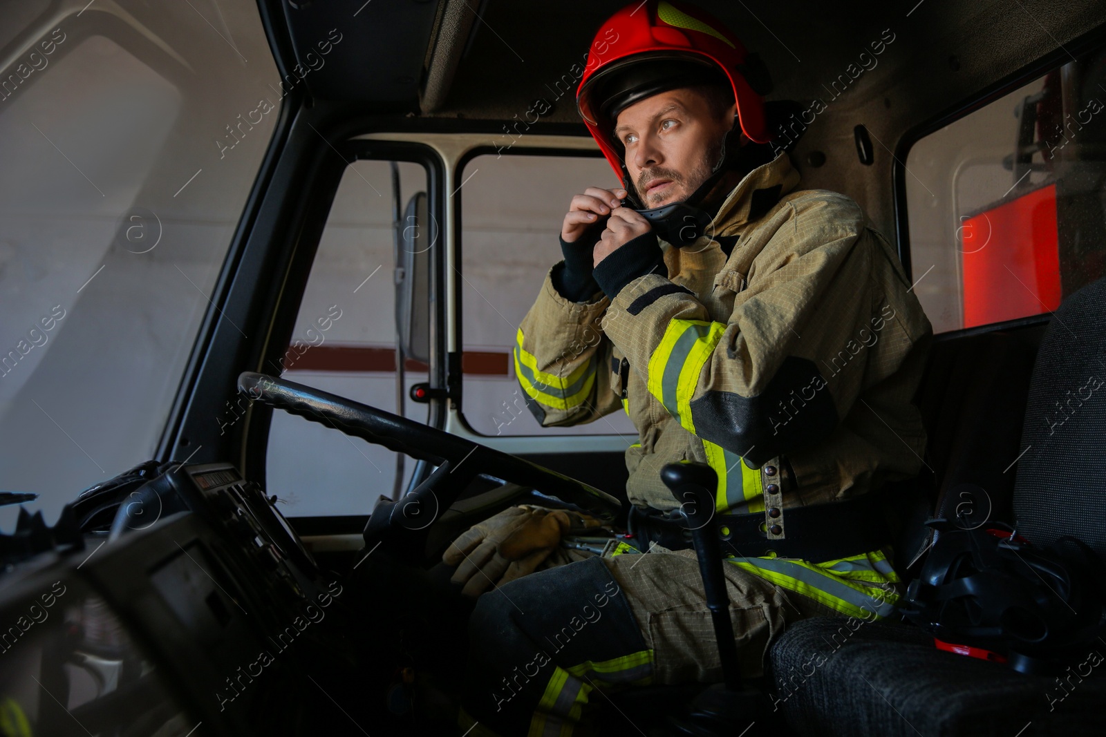 Photo of Firefighter in uniform wearing helmet inside fire truck