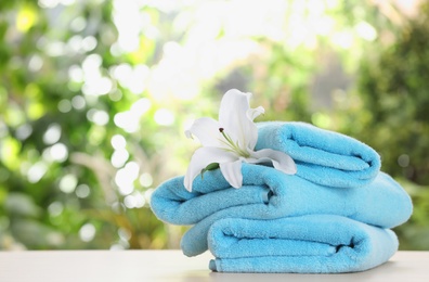 Stack of clean soft towels and flower on table against blurred background. Space for text