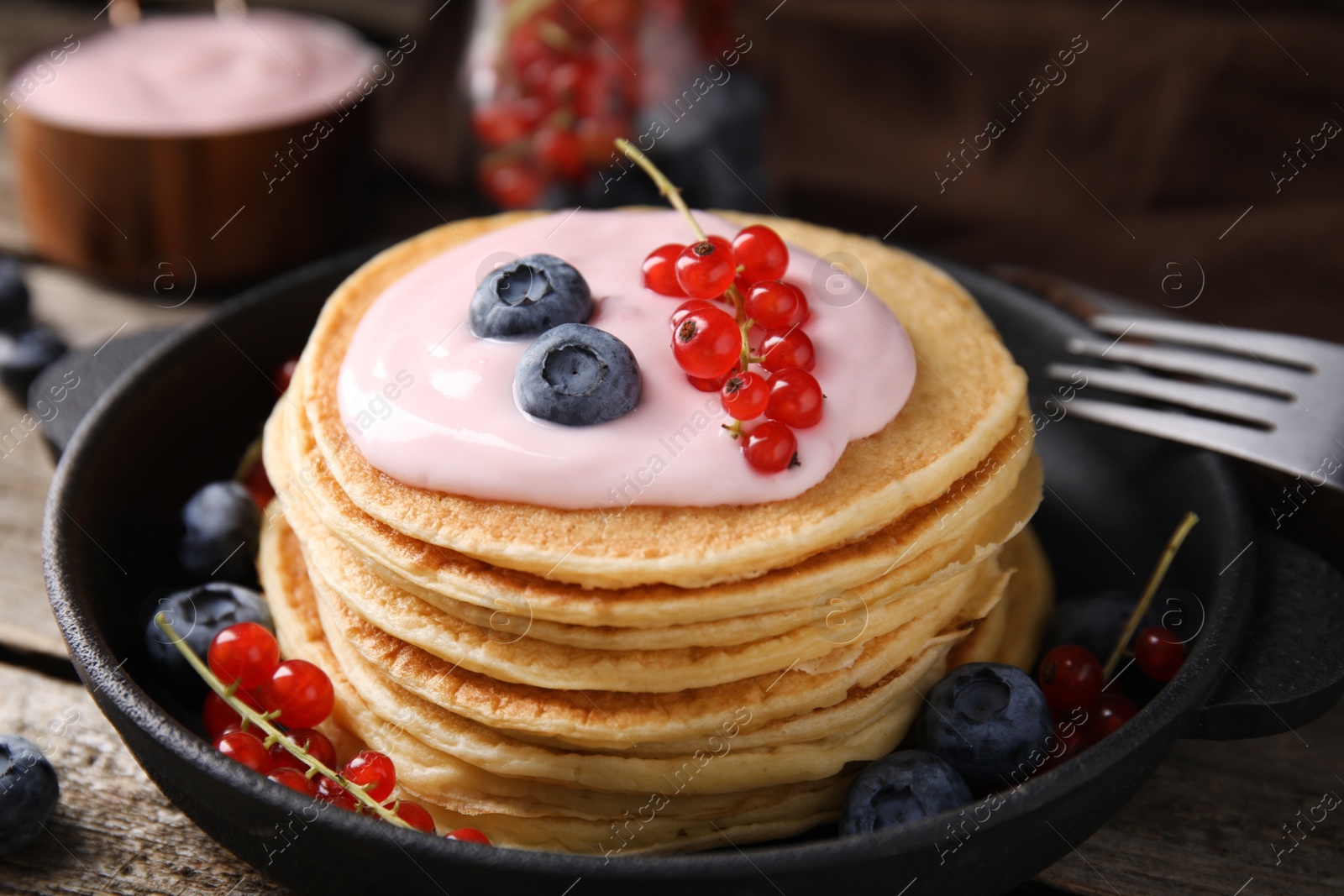 Photo of Tasty pancakes with natural yogurt, blueberries and red currants on wooden table, closeup