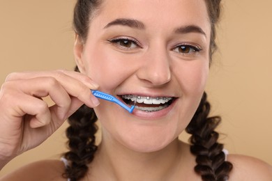 Photo of Smiling woman with dental braces cleaning teeth using interdental brush on beige background, closeup