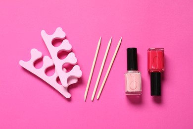 Photo of Nail polishes, orange sticks and toe separators on pink background, flat lay