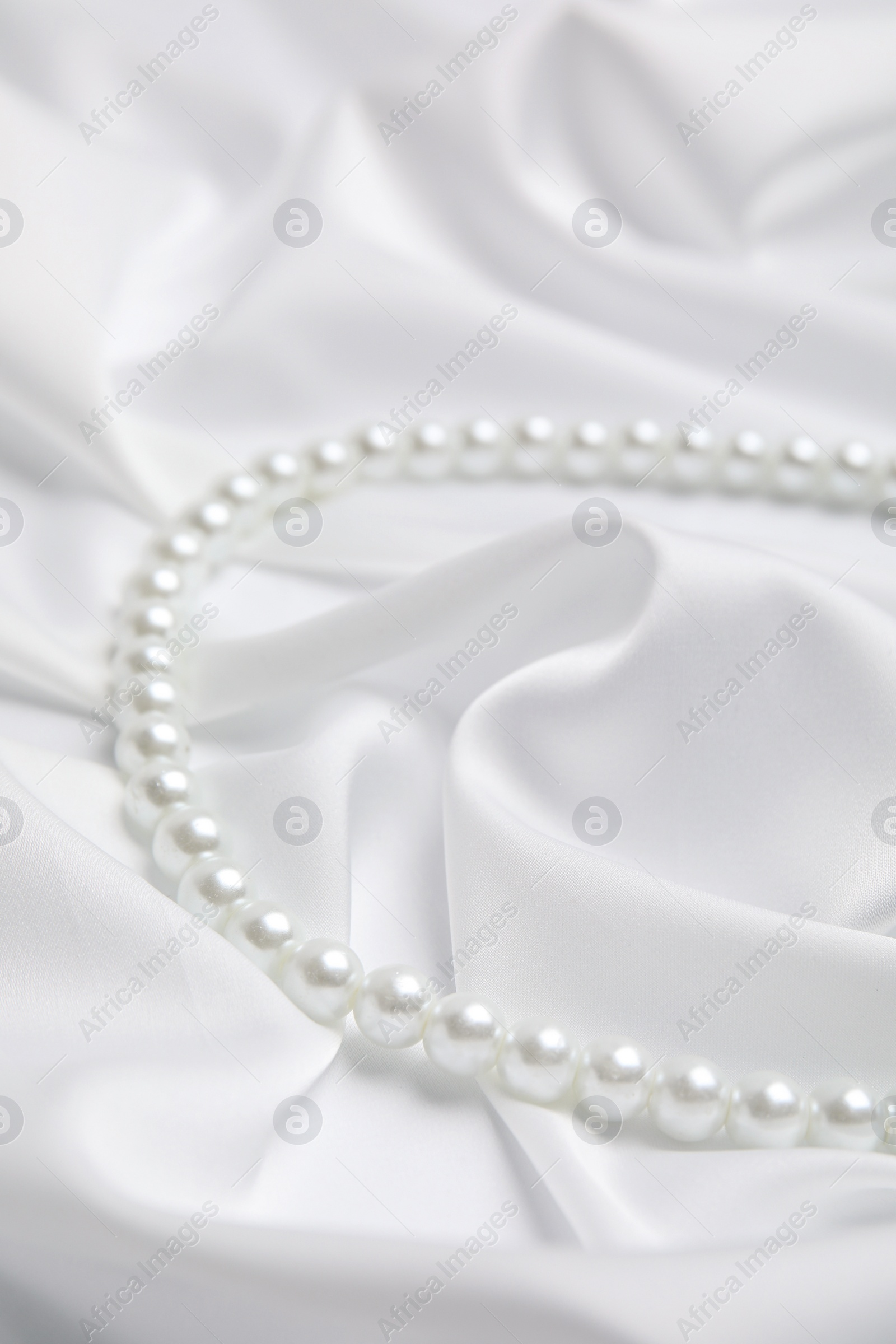 Photo of Beautiful pearls on white silk, closeup view